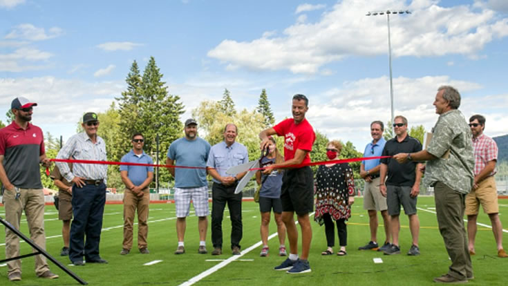 stakeholders cutting red ribbon on football field at grand opening